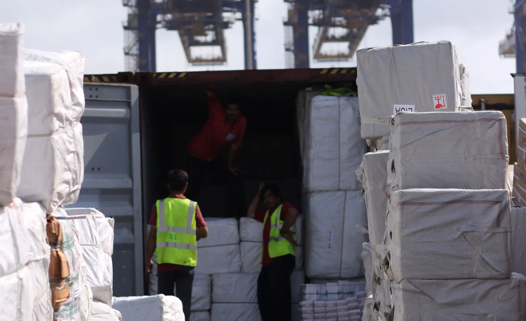 Wrapped freight beside workers at an open shipping container